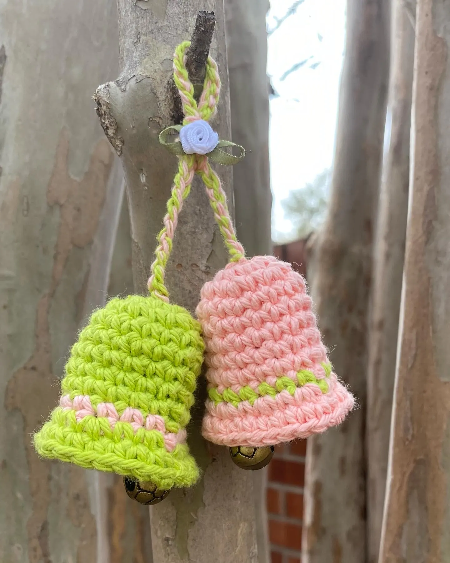 Two small pastel crochet bell keychains hanging on a branch