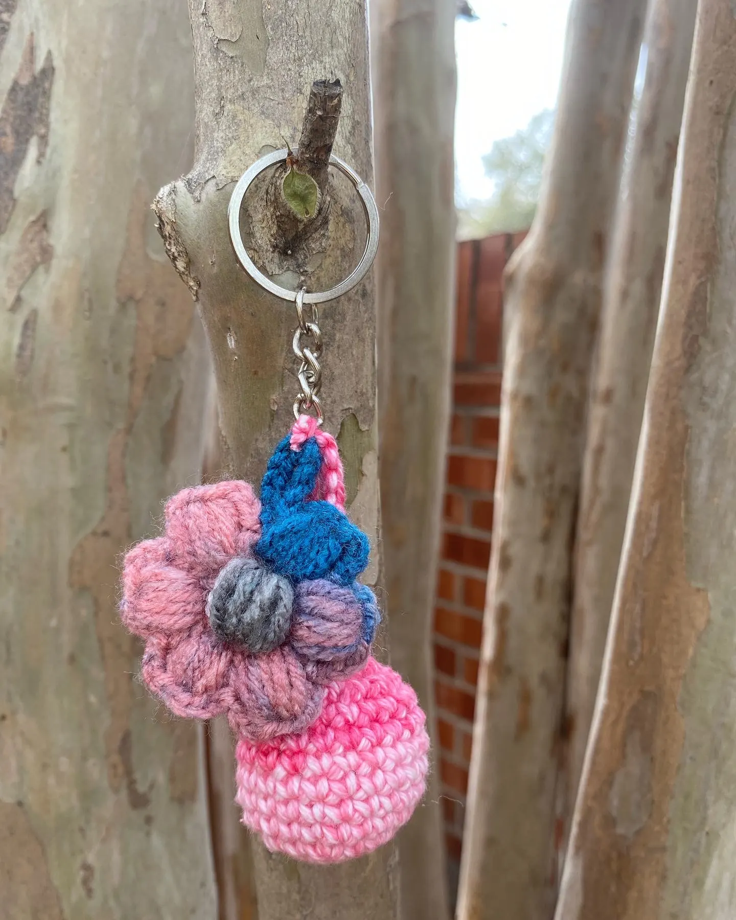 Pink and blue flower crochet keychain hanging on a tree branch