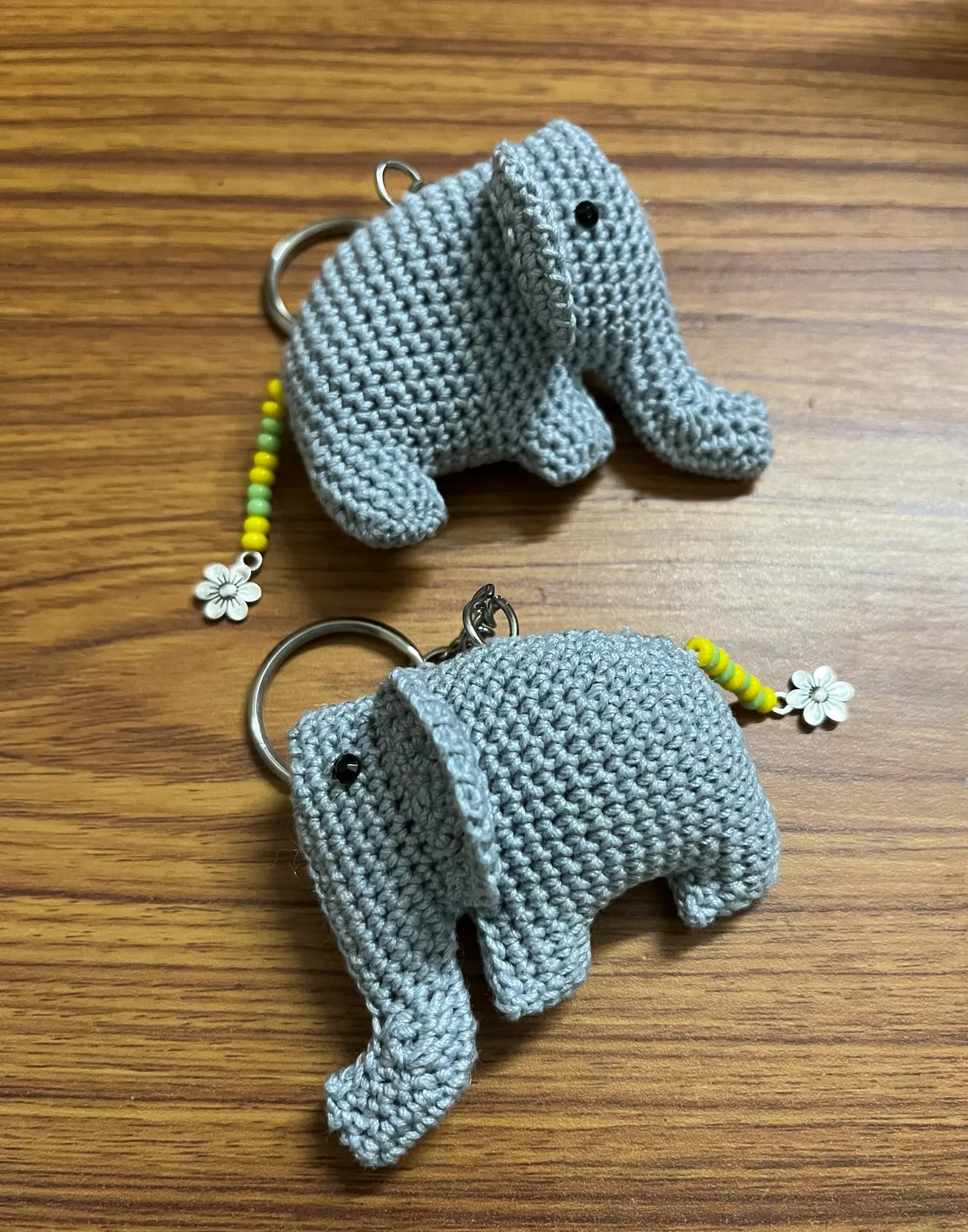 Two gray elephant crochet keychains on a wooden table