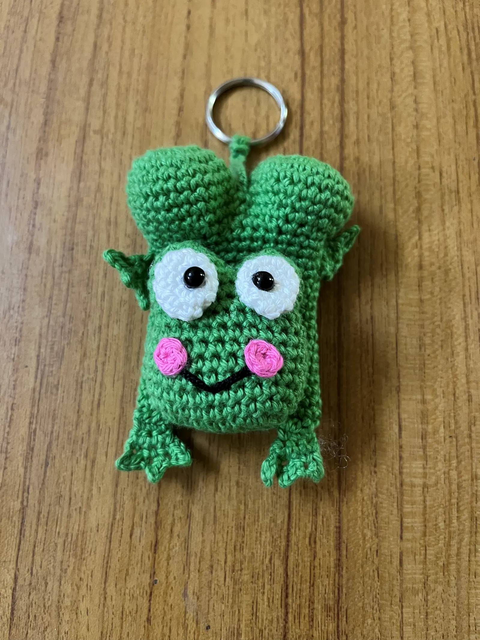 Green frog crochet keychain on wooden background