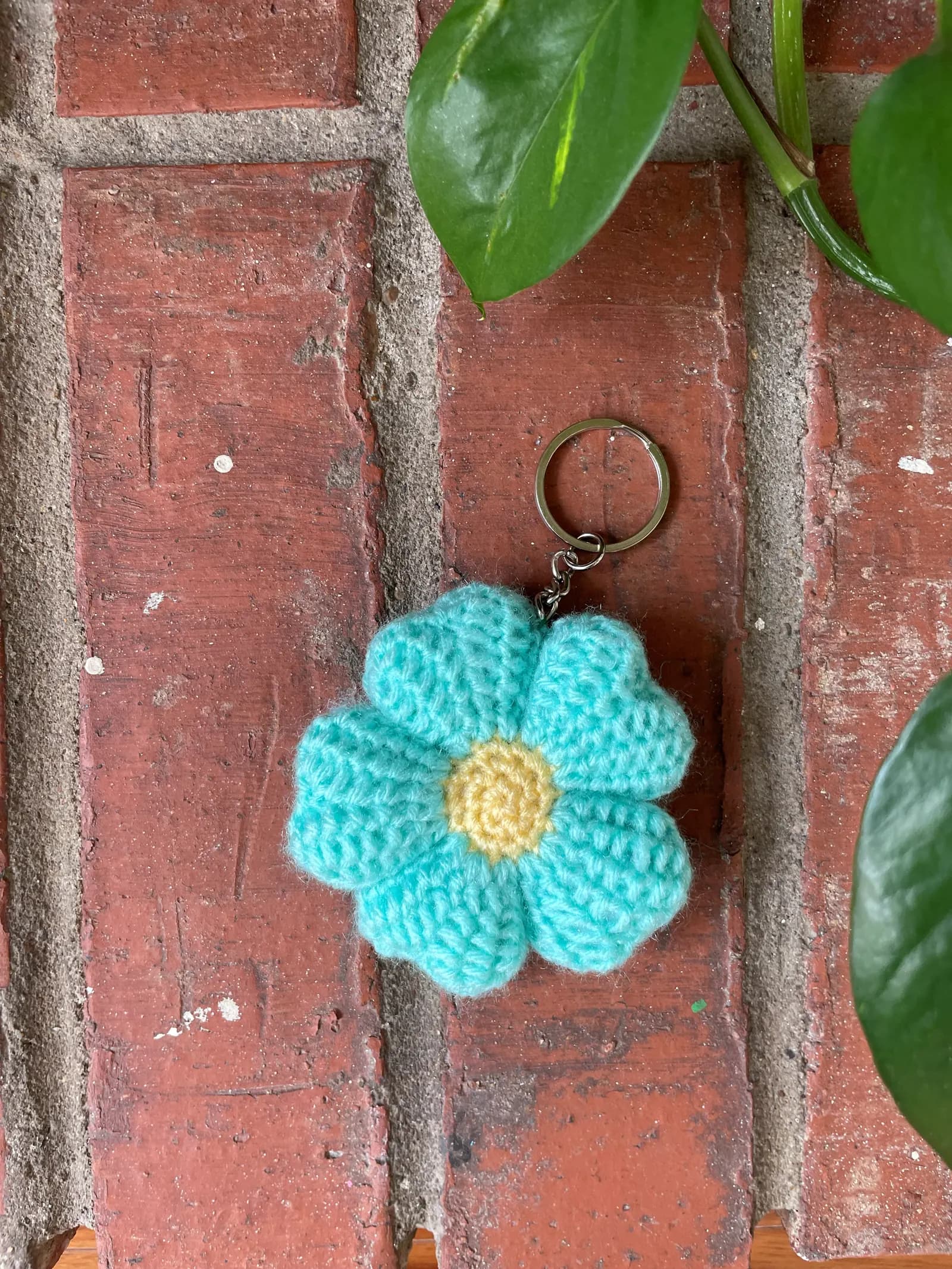 Aqua blue flower crochet keychain on brick wall